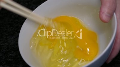 Slow motion of woman stirring egg by chopstick inside bowl