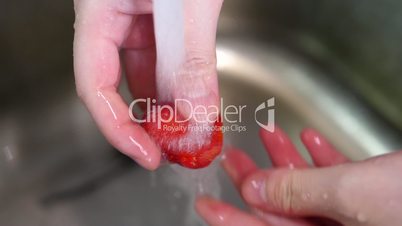 Slow motion of woman washing strawberry in kitchen sink under tap water