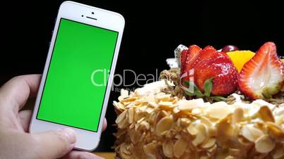 Motion of fruit birthday cake and hand holding green screen phone on a black background