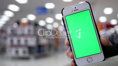 Woman holding green screen mobile phone on beautiful blurred lighting background inside Walmart store