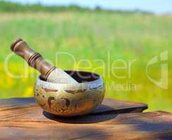 Copper Tibetan singing bowl on a brown wooden background, blurre