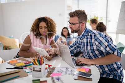 Male and female executives discussing over digital tablet in the office