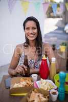 Portrait of beautiful woman holding beer bottle while having snacks