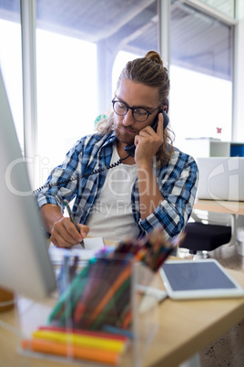 Male executive talking on phone while working at his desk