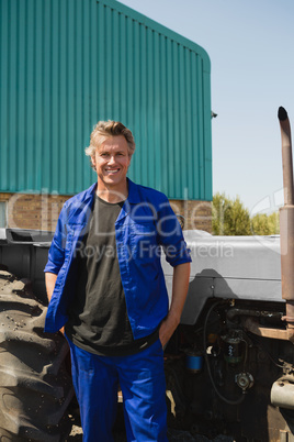 Worker standing with hands in pocket near tractor