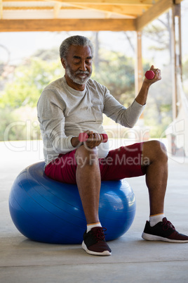 Senior man exercising with dumbbells on exercise ball in the porch