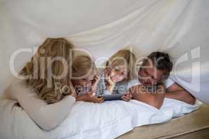 Happy family using digital tablet under blanket in bedroom