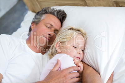 Father and daughter sleeping together on bed in bedroom