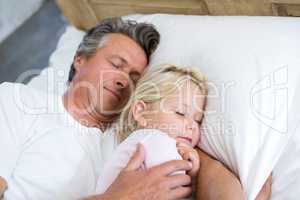 Father and daughter sleeping together on bed in bedroom