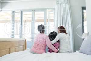 Rear view of family sitting together with arm around on bed