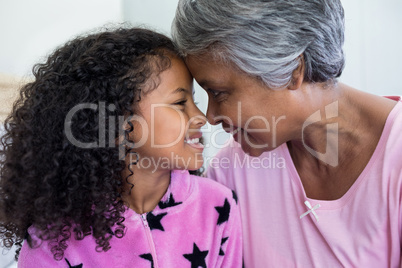Smiling granddaughter and grandmother sitting face to face in bedroom