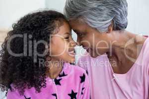 Smiling granddaughter and grandmother sitting face to face in bedroom