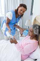 Female doctor measuring blood pressure of senior woman in bedroom
