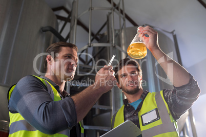 Low angle view of coworkers examining beer in beaker