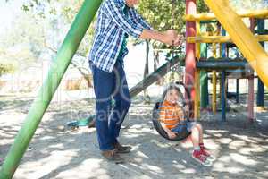 Low section of father pushing son sitting on swing