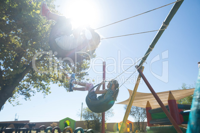 Siblings swinging against sky during sunny day