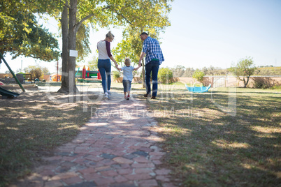 Parents and son holding hands while walking at park