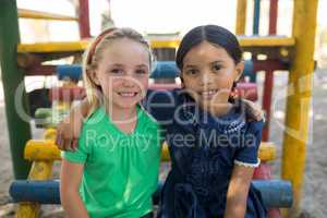 Portrait of friends with arms around sitting on jungle gym