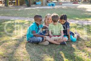 Boy using digital tablet while sitting with friends on grassy field