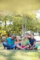 Portrait of cheerful children with arms around sitting at park