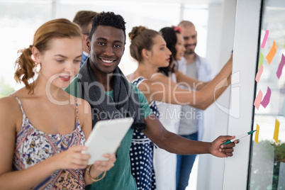 Female executive using digital tablet while male executive pointing at sticky notes
