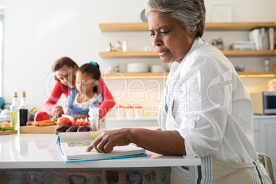 Senior woman looking at recipe book in kitchen