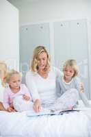 Kids and mother reading story book in bedroom