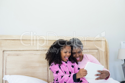 Grandmother and granddaughter taking selfie on digital tablet in bed room