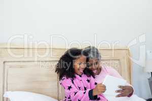Grandmother and granddaughter taking selfie on digital tablet in bed room