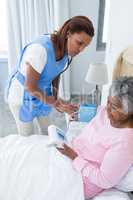 Female doctor measuring blood pressure of senior woman in bedroom