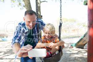 Father taking selfie with son sitting on swing