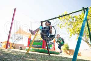 Girls swinging at playground against sky