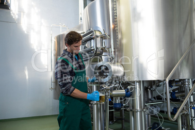 Male worker taking beer from storage tank at factory