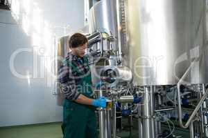 Male worker taking beer from storage tank at factory