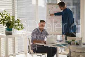 Male executive using laptop while coworker writing on flip chart