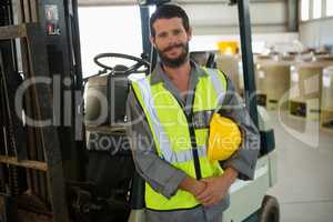 Smiling worker standing near forklift in factory