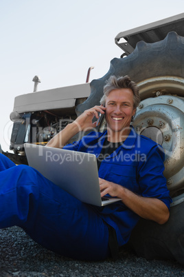 Worker talking on mobile phone while using laptop on a sunny day