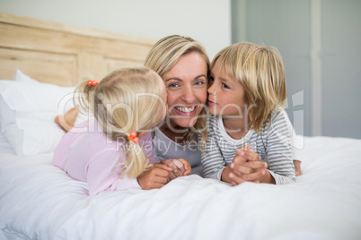 Kids kissing mother on her cheeks in bed room