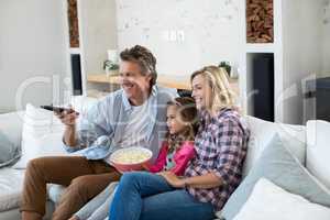 Smiling family watching television while having popcorn in living room