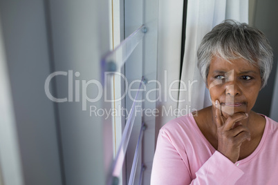 Thoughtful senior woman looking through window in bed room