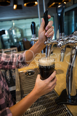 Cropped hands of barmaid pouring drink from tap in glass at counter