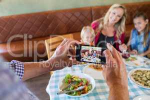 Cropped hand of father photographing family at restaurant