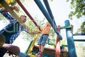 Father looking at son walking on jungle gym at playground