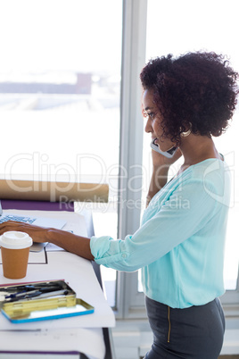 Female architect talking on mobile phone while working over laptop