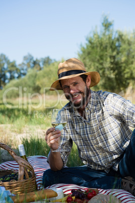 Portrait of man sitting with a glass of wine on picnic blanket