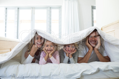 Portrait of happy family lying under blanket on bed in bedroom