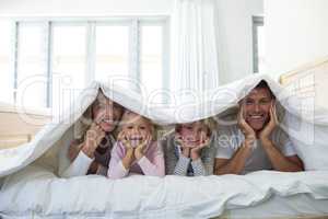 Portrait of happy family lying under blanket on bed in bedroom