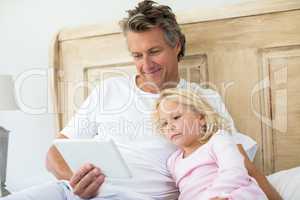 Smiling father and daughter using digital tablet on bed