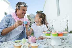 Smiling father and daughter in fairy costume toasting cup of tea