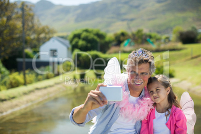 Smiling father and daughter in fairy costume taking selfie on mobile phone
